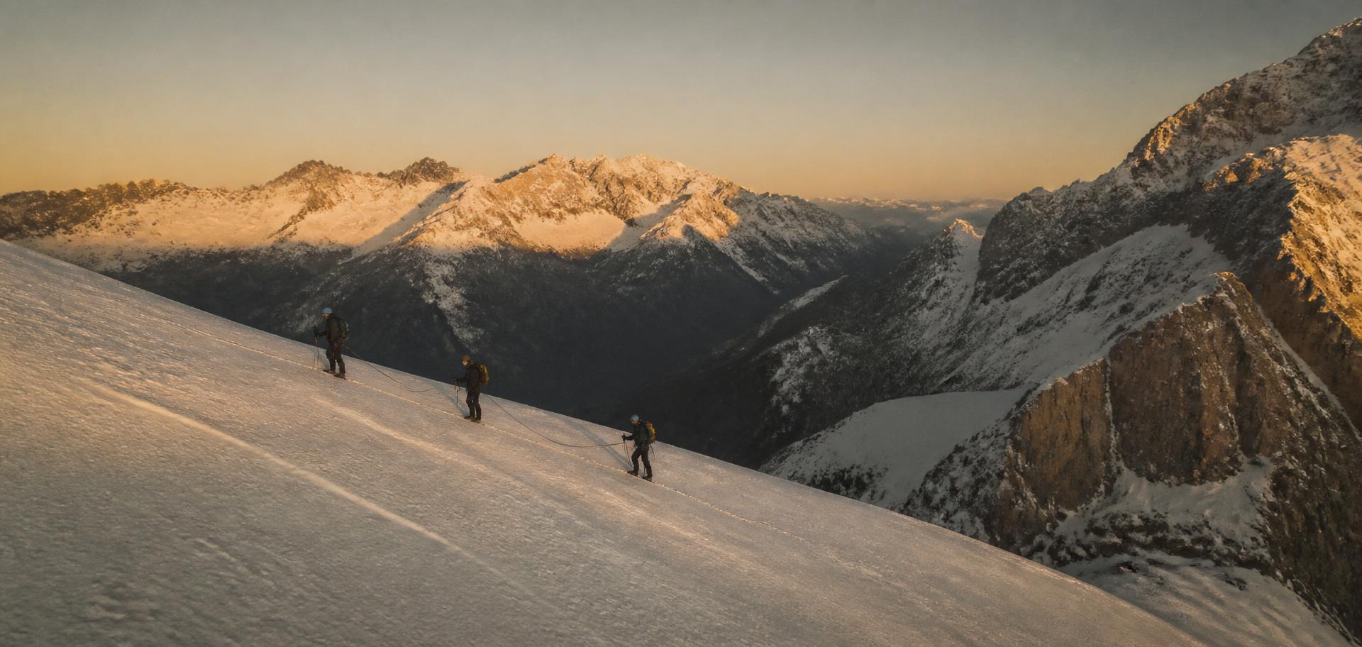 Grupo de alpinistas encordados en una arista nevada del Pirineo al amanecer